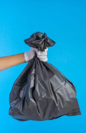 The male hand holding a garbage bag and a blue background.